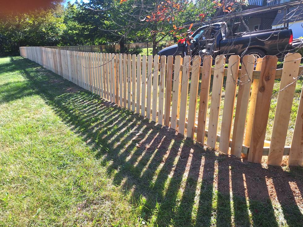 A new cedar picket fence running the length of a lawn toward a parked truck, the tops held level the whole way down.