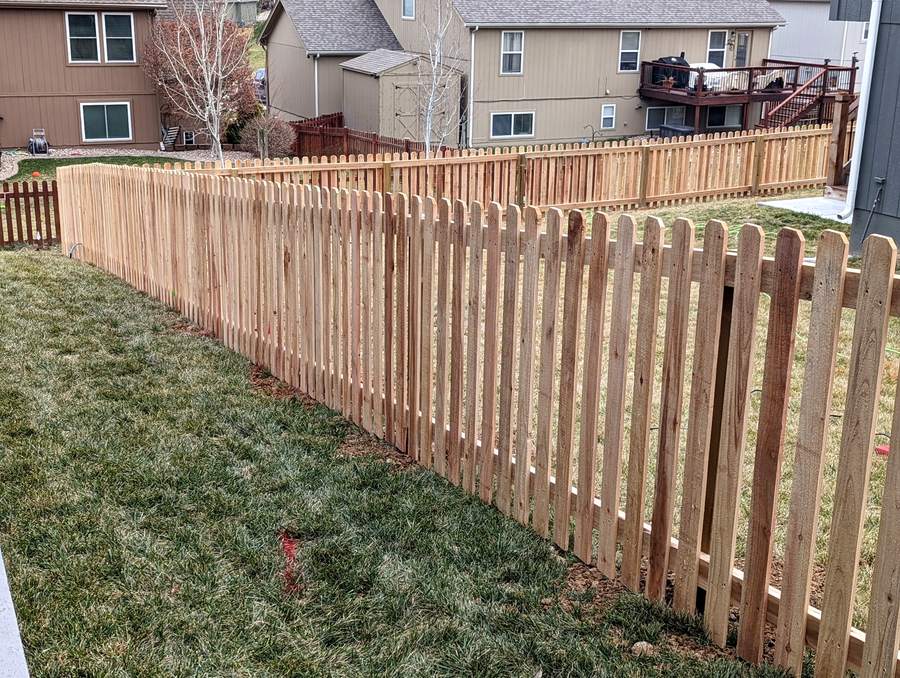 A cedar picket fence running downhill across a back yard with the panels stepped.