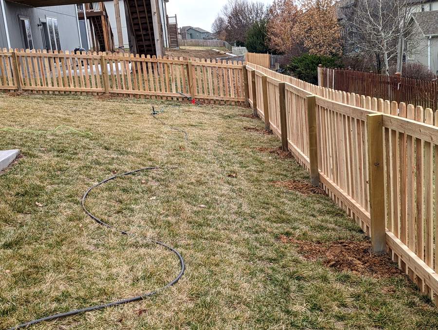 A cedar picket fence enclosing a back yard, tops running level from post to post.