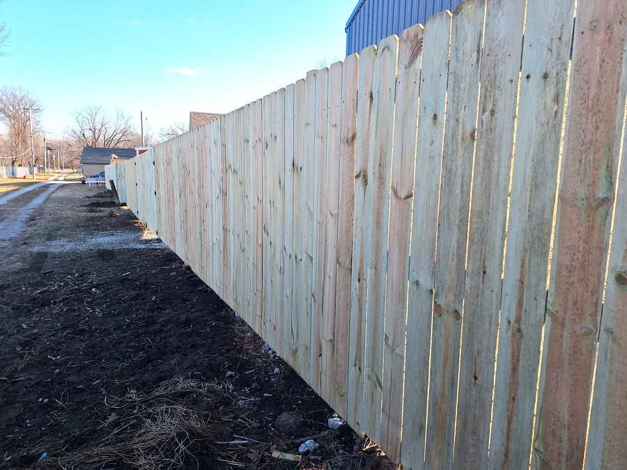 A tall solid cedar privacy fence running the length of a lot beside a strip of turned soil.