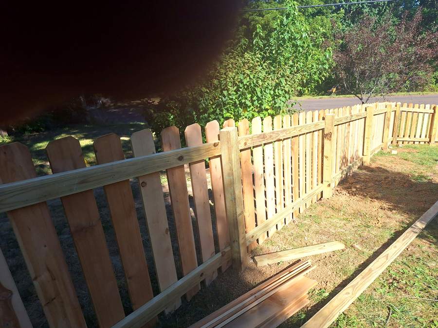 A spaced picket fence turning an angled corner across a back lawn with a gate in the line.