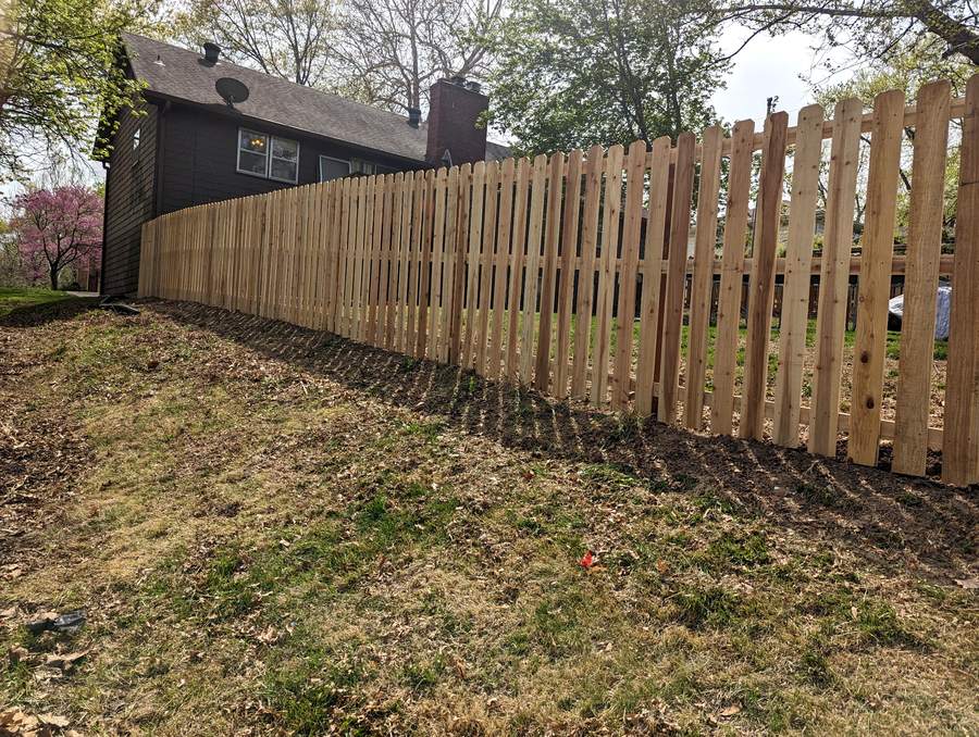 A shadowbox cedar fence running along a back tree line beside a dark brown house.