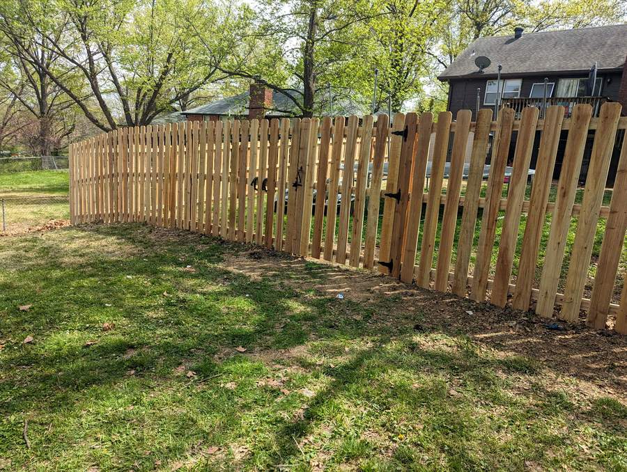 A shadowbox cedar fence with boards alternating on both faces of the rails, running across a back yard toward a dark house.