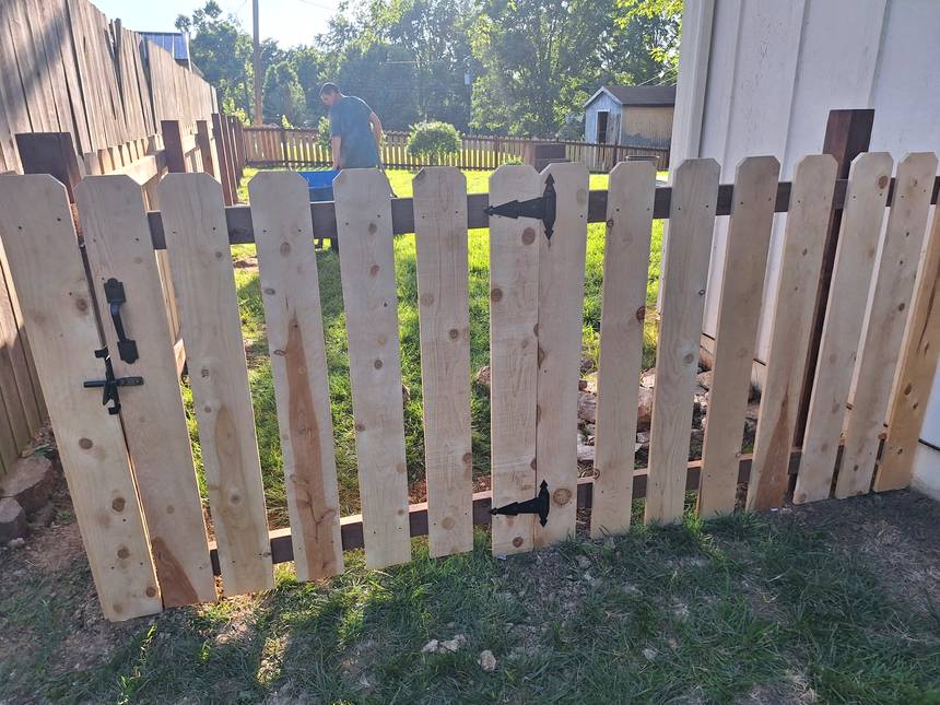 A cedar picket gate hung on ornate black antique style strap hinges with a black drop rod and latch on the post.