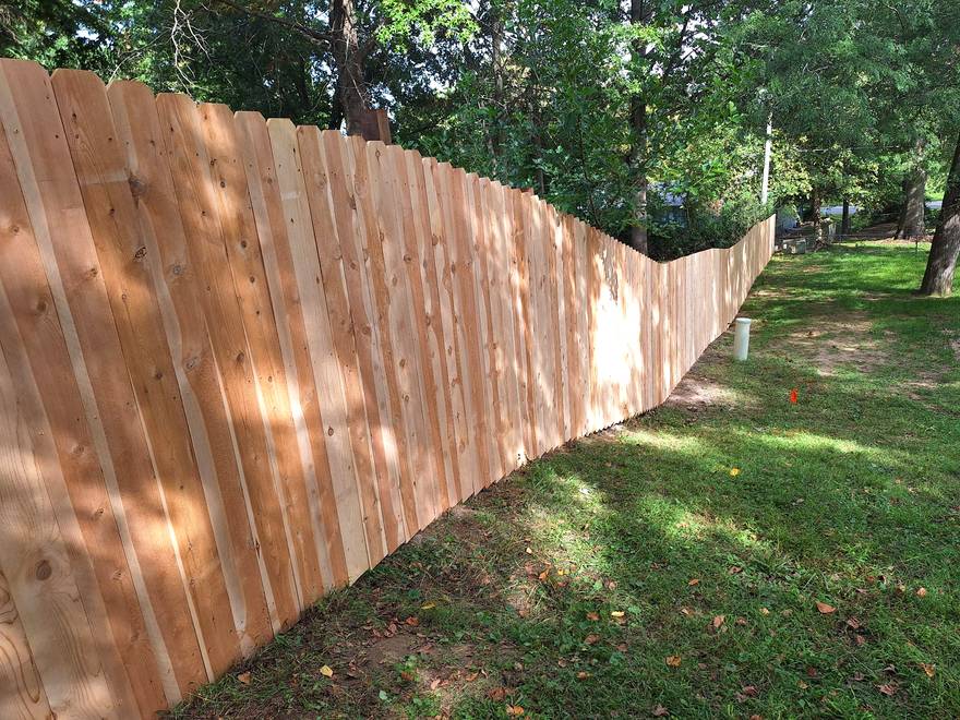 A solid cedar privacy fence carried down a steep grassy bank, the panels stepped so the top line stays even.